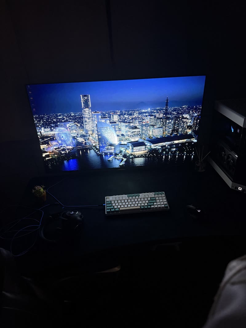 AORUS FO48U front view with daytime cityscape wallpaper, white SFF PC visible to the right, mechanical keyboard, succulent on desk corner
