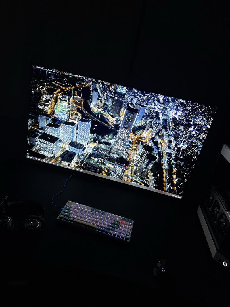 Overhead view of AORUS FO48U with Tokyo aerial night cityscape wallpaper, panel filling the frame, peripherals visible at the bottom