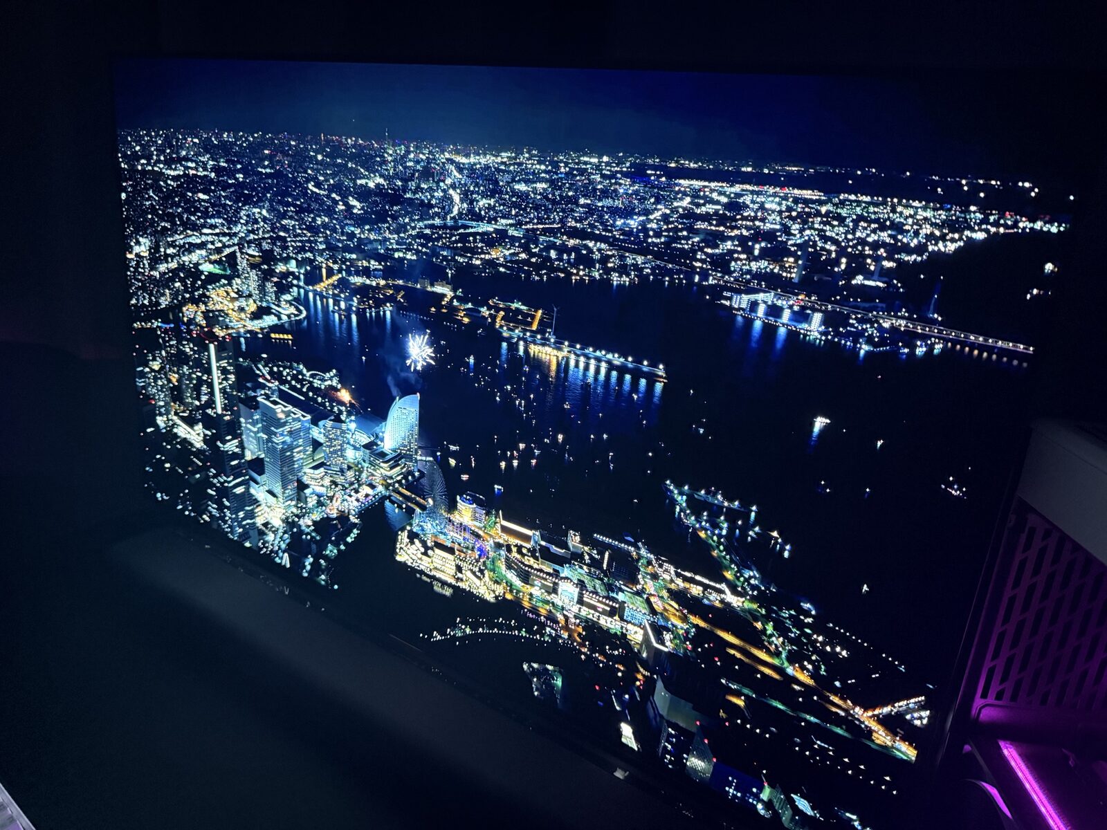 AORUS FO48U displaying Yokohama harbor night scene with mid-cityscape glow on left, harbor water in lower frame, and PC side panel with purple RGB visible at the right edge