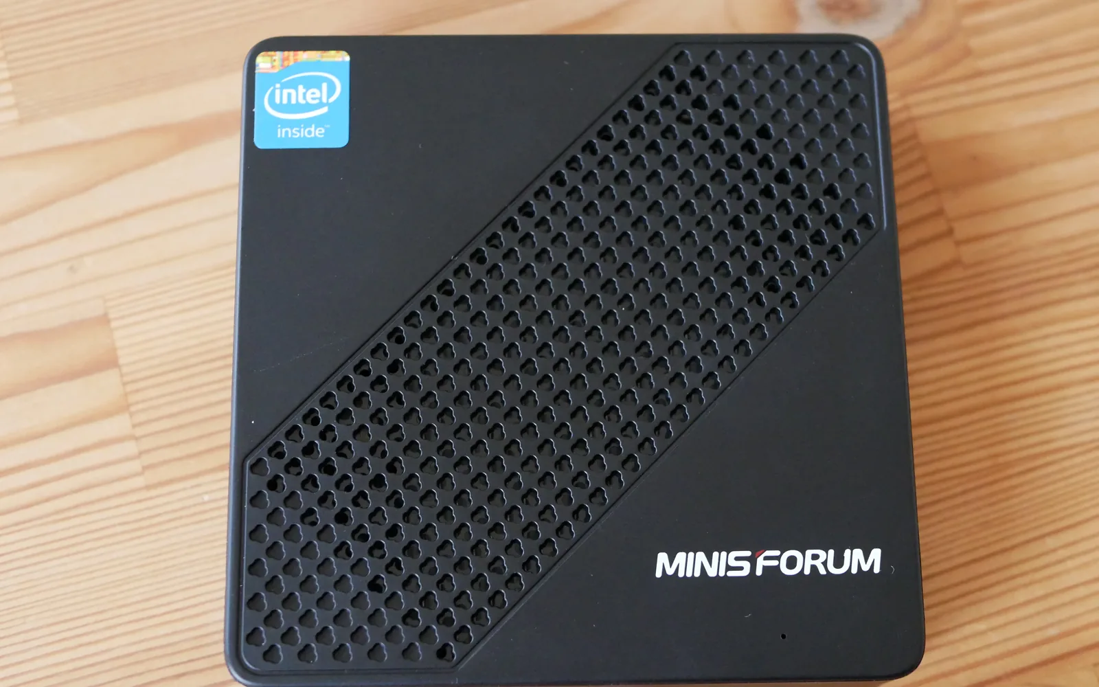 A black Minisforum mini PC seen from above on a pine desk, an Intel badge on its perforated lid and the Minisforum name in the corner