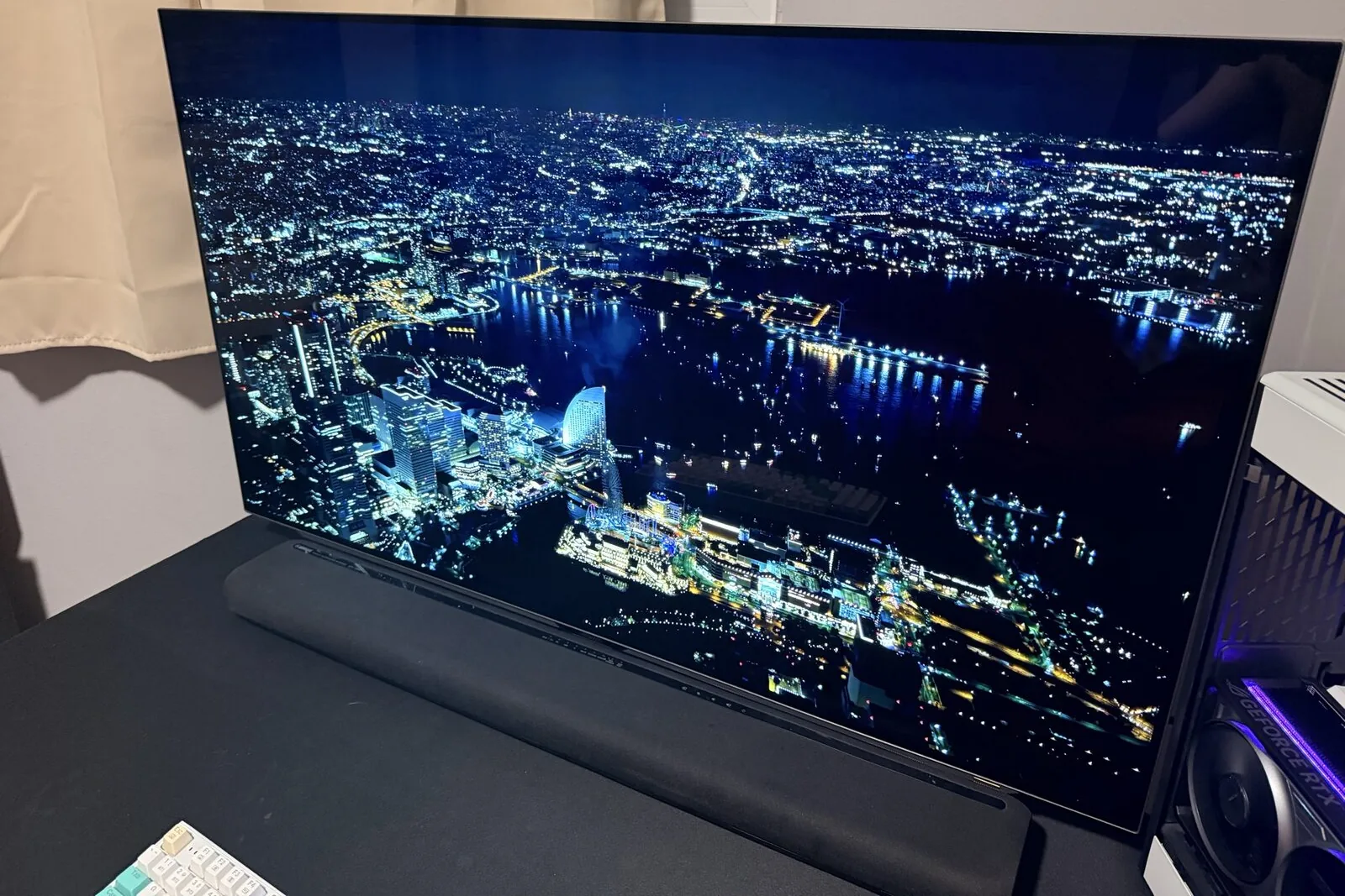 An AORUS FO48U OLED monitor on my desk with a black fabric soundbar in front of its stand, the bar rising into the lower edge of the screen