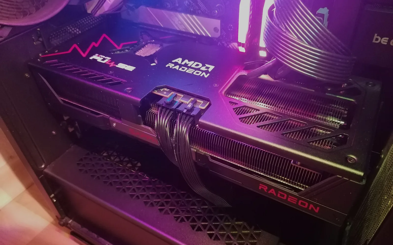 An AMD Radeon RX 9070 XT graphics card installed in a PC case, its power cables connected and the interior lit by magenta RGB lighting