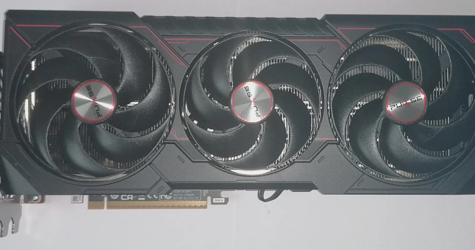 A Sapphire Pulse Radeon RX 9070 XT graphics card lying fan-side up on a white surface, its three Pulse-badged fans and red trim facing the camera