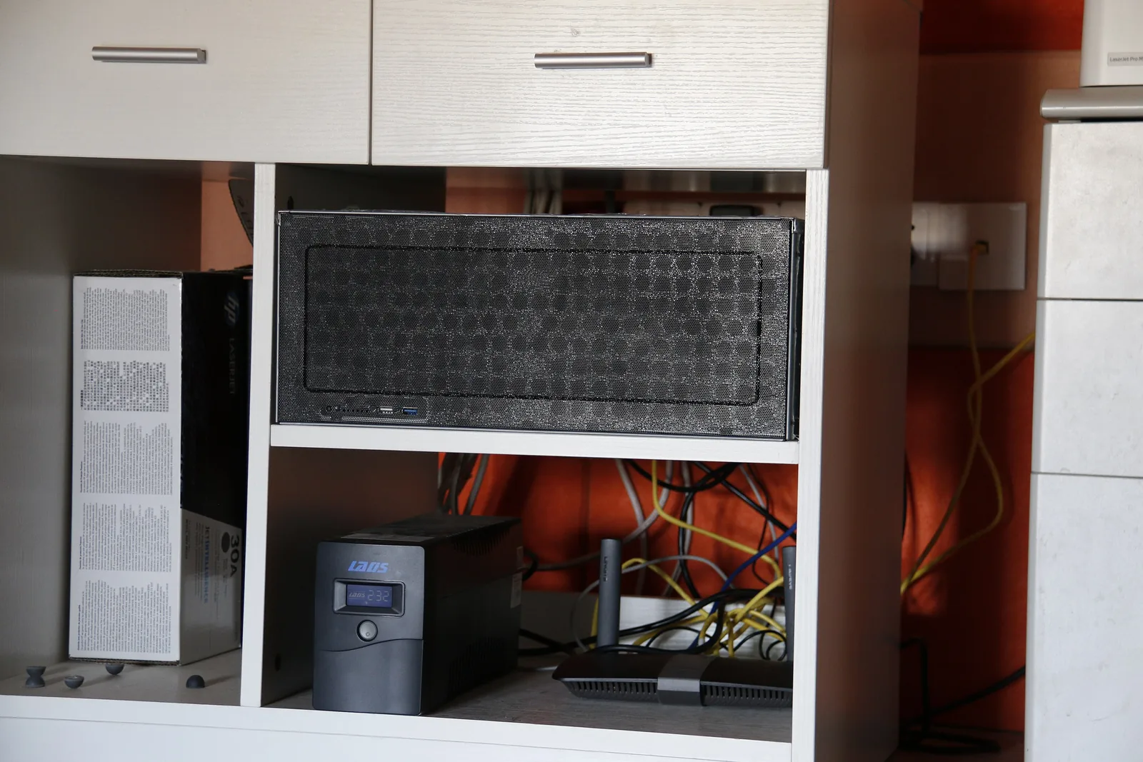 A home self-hosting shelf built into a kitchen cabinet: a tower server above, an uninterruptible power supply and a small router below