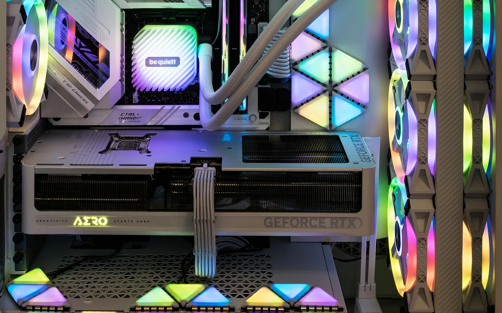 The inside of a white gaming PC: an RGB-lit all-in-one cooler, a be quiet! pump head, a GeForce RTX graphics card and illuminated case fans