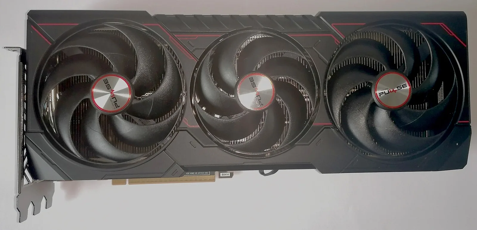 A Sapphire Pulse Radeon RX 9070 XT graphics card photographed from above on a white surface, its three cooling fans and PCIe connector visible
