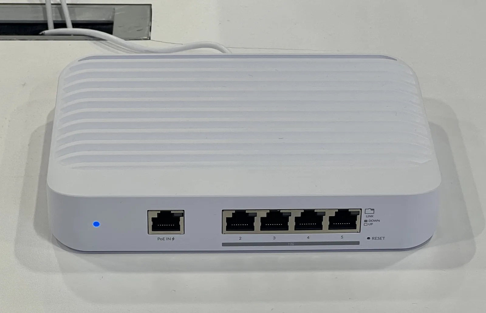 A white Ubiquiti UniFi Switch Flex XG ten-gigabit switch on a desk, its four RJ45 ports and PoE input visible along the front edge