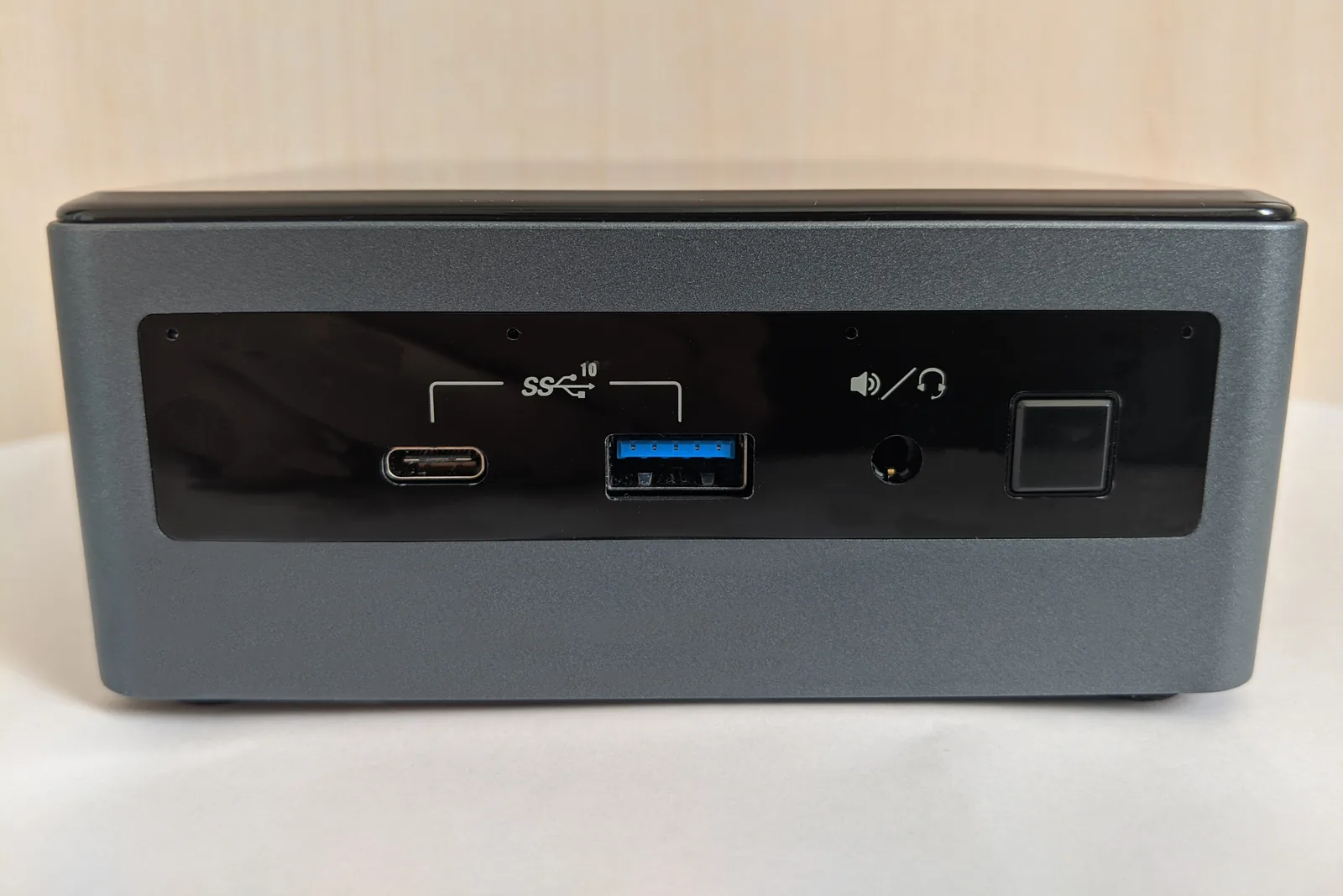 An Intel NUC10 mini PC seen from the front on a light desk: a USB-C port, a blue USB-A port, a headphone jack and the power button on its black front panel