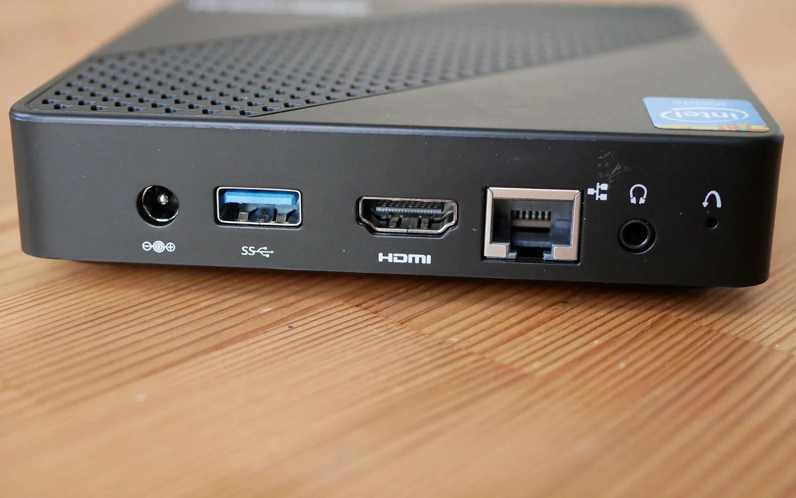 The rear panel of a black Minisforum N40 mini PC on a pine desk, showing its power, USB, HDMI, Ethernet and audio ports